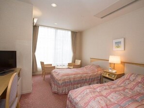 Habitación de hotel con dos camas, un escritorio, una silla, un televisor y una ventana con cortinas.