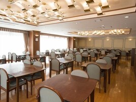 Un comedor de hotel con varias mesas y sillas, ventanas amplias y un diseño moderno de techo.