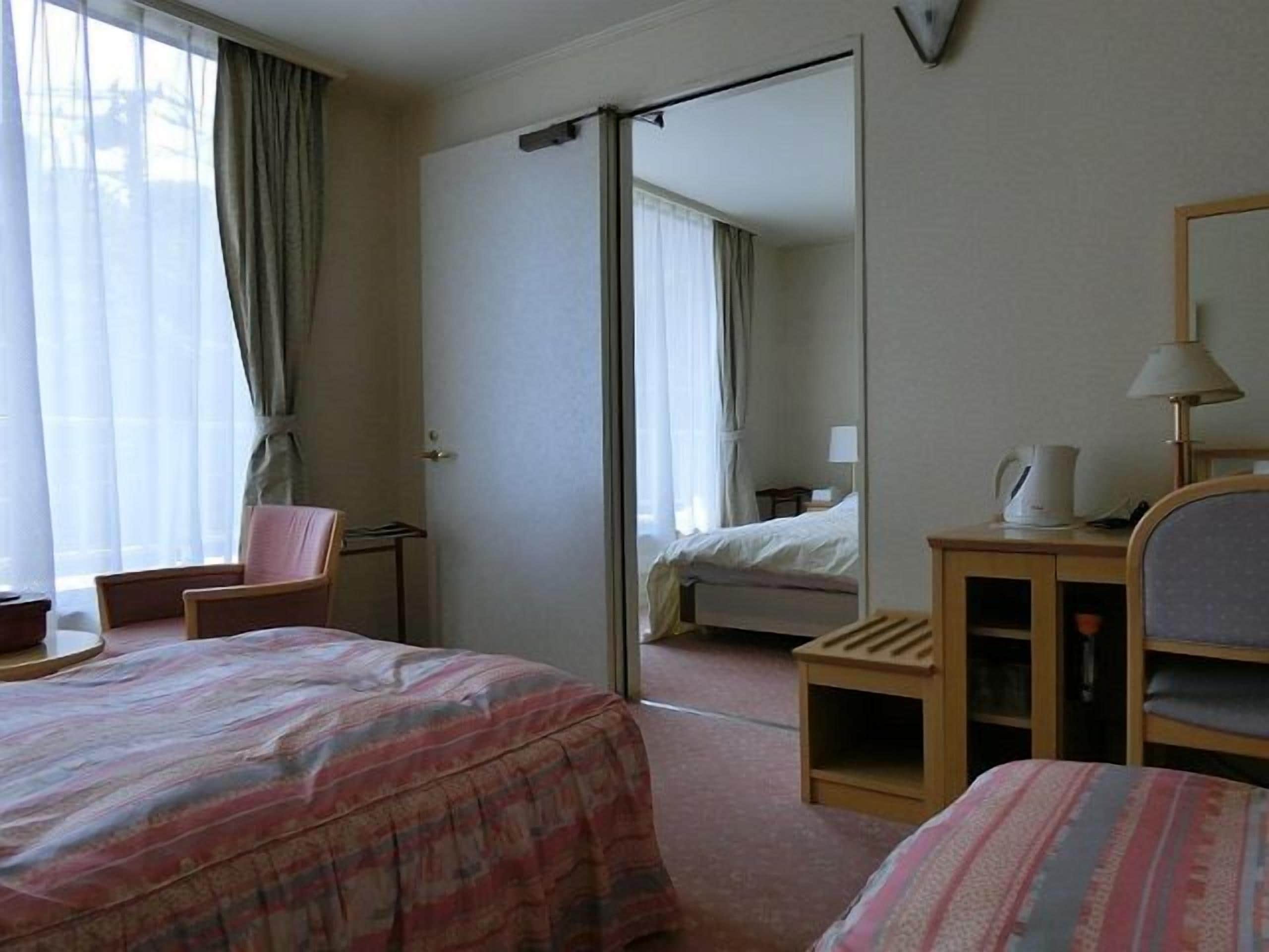A hotel room with a bed, a chair, a desk, a mirror, and a window with curtains.