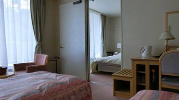 A hotel room with a bed, a chair, a desk, a mirror, and a window with curtains.