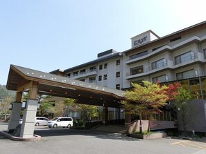 A multi-story hotel with a covered entrance, a parking area, and a landscaped garden with trees. - Shiobara Onsen Hotel New Momiji (Nasushiobara)