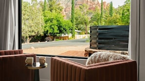 A room with a large window offering a view of a mountainous landscape, a wooden bench, and a small table with two cups.