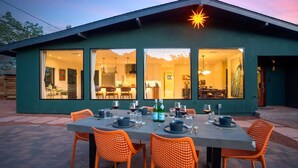 A modern house with large windows, a dining area with orange chairs, and a table set for a meal.