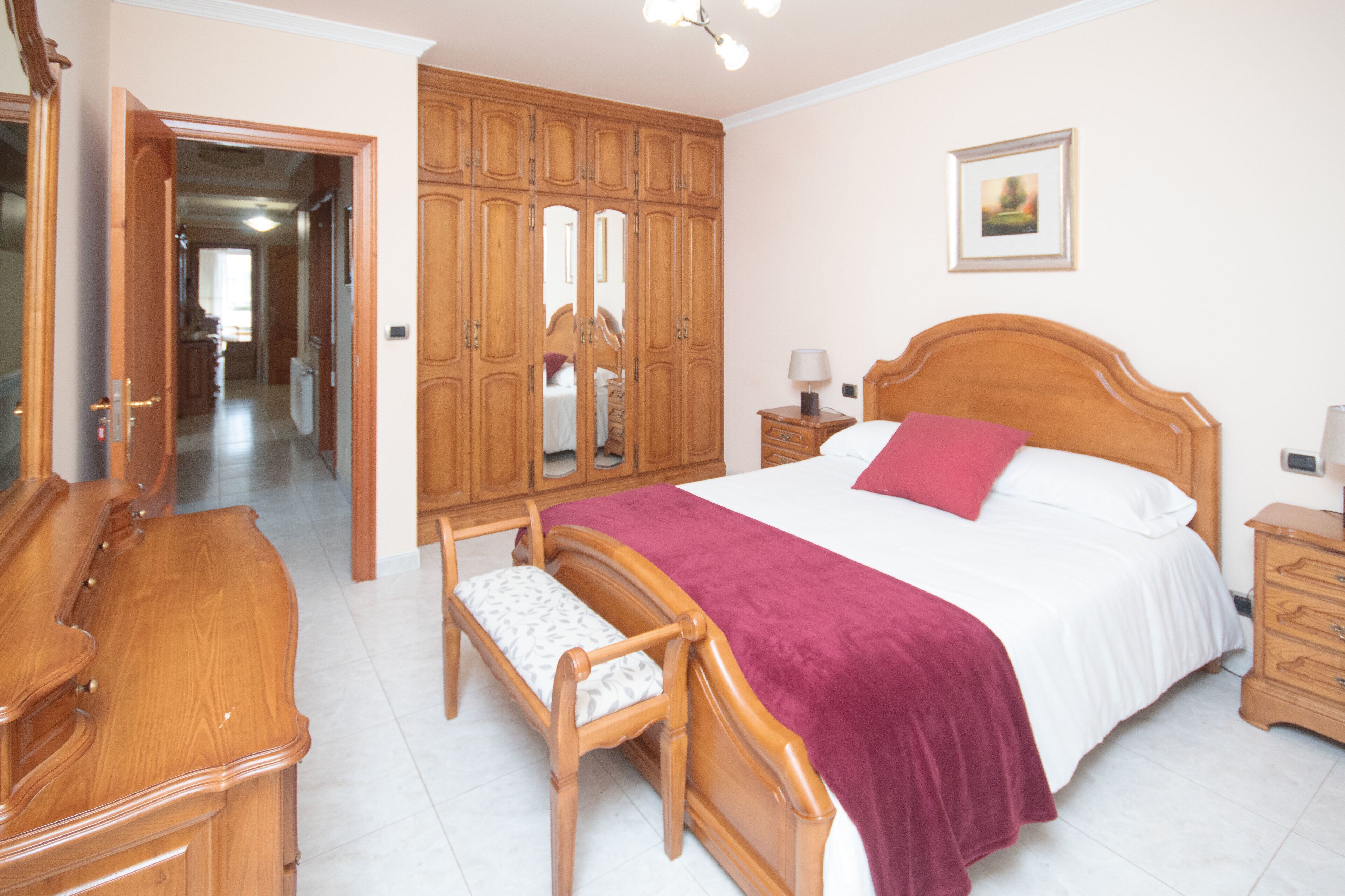 Une chambre à coucher avec un lit en bois, une table de chevet, une commode, un banc et une armoire.