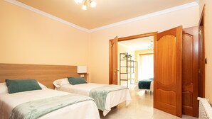 A hotel room with two beds, a wooden headboard, a white radiator, and a door leading to another room. - AG Flat Rio Miño Carballo, 700m from the center (Carballo)