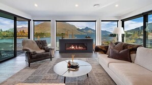 Una sala de estar moderna con chimenea, dos sofás, una mesa de centro y grandes ventanas con vistas a la montaña.