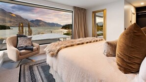 Un dormitorio con una cama grande, una silla, un espejo y vistas a un lago y montañas.