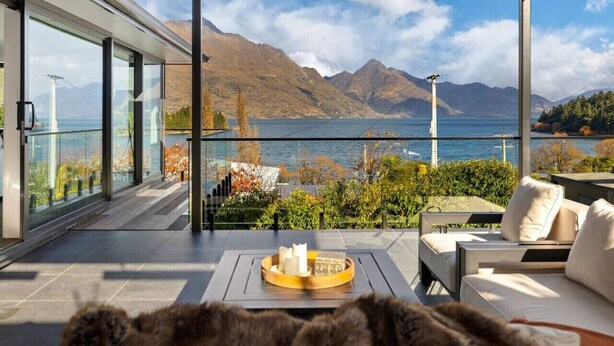 Un área de estar moderna al aire libre con vistas a un lago y montañas.