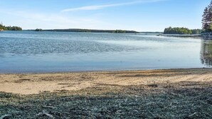 A calm lake with a sandy beach and dense forest in the background. - Oceanfront Cottage • Firepit + Beach • Near Acadia & Bar Harbor  (Milbridge)