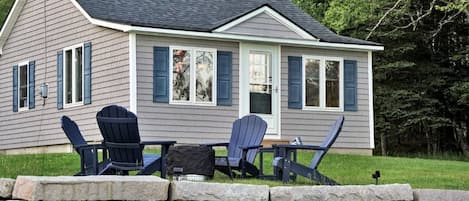 Una casa con un muro de piedra frontal, un patio cubierto con sillas Adirondack y fachada revestida de color gris.