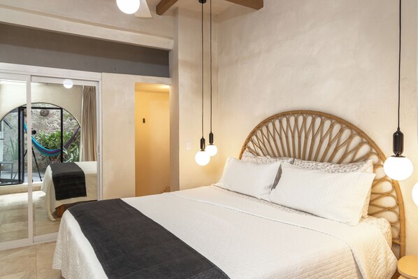 A bedroom with a large bed, a wooden headboard, and a glass door leading to a balcony with a hammock.