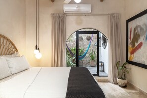 A bedroom with a bed, a potted plant, and a view of a garden through a glass door.
