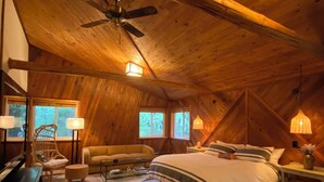 A cozy bedroom with a wooden ceiling, a bed with striped bedding, a chair, a small table, and two windows. - Naked Elk Lodge: 4 Bdrms, Hot Tub, Projector TV near Mt. Rainier (Packwood)