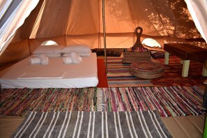 A tent with a bed, pillows, a bench, and a woven basket.