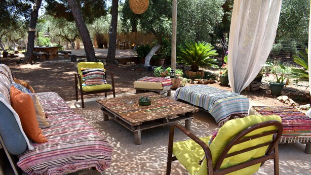 An outdoor seating area with wooden furniture, cushions, and potted plants. - Private Eco Tent in Skiaxtro Cocoon Retreat (Marathopoli)