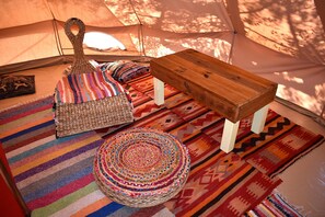 Interior de una tienda de campaña con un banco de madera, un otomano tejido de colores y alfombras estampadas.