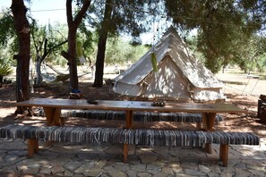 A wooden picnic table with benches, a tent, and a hammock in a wooded area.