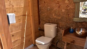A small, rustic bathroom with a wooden door, a white toilet, a stone wall, and a wooden shelf with a metal bowl. - Private Eco Tent in Skiaxtro Cocoon Retreat (Marathopoli)