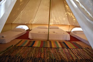A cozy tent with three beds, each with white linens and pillows. A colorful striped rug is placed in front of the beds.