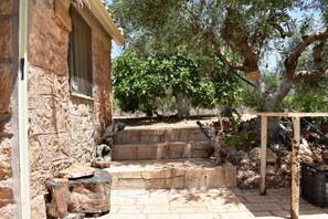 A stone building with a window, a staircase leading to a wooden deck, and a tree in the background.