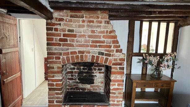 Una chimenea de ladrillo rústica con repisa de madera, una mesa de madera con un jarrón de flores y una puerta de madera.