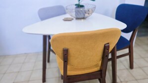 Un comedor con una mesa blanca, una silla azul y una silla color mostaza, y una planta sobre la mesa.