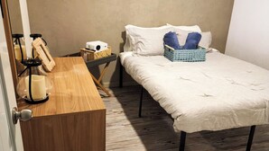Un dormitorio pequeño y ordenado con un escritorio de madera, una cama con un cesto azul y una estantería fijada a la pared.