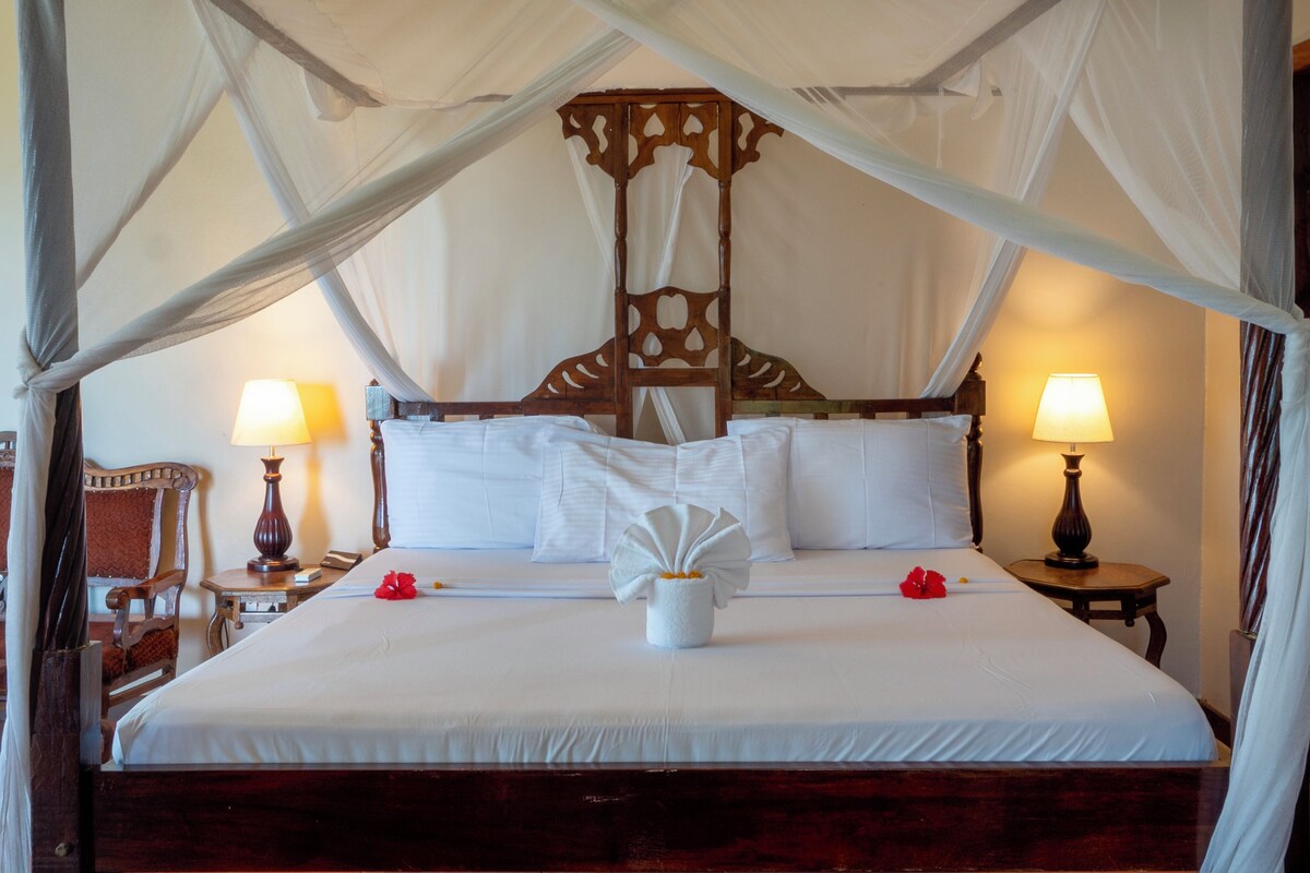 A large bed with a canopy, two bedside lamps, and a wooden headboard.