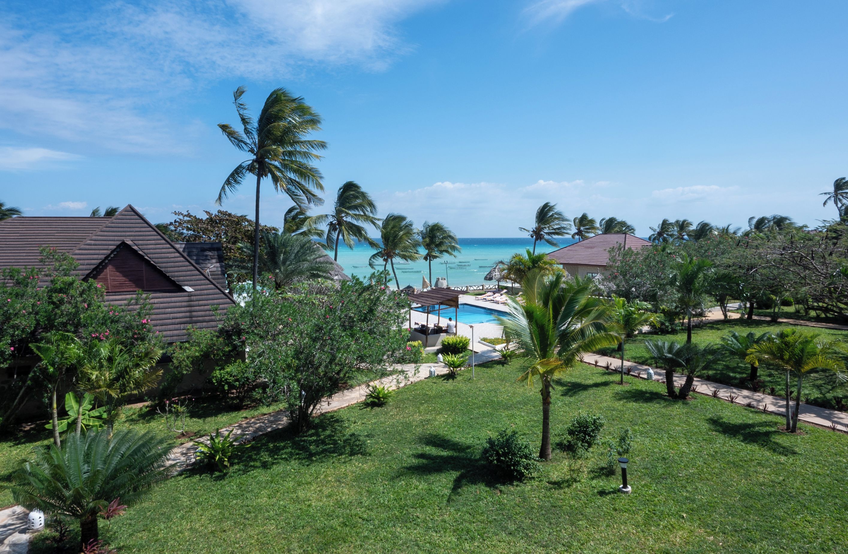 A resort with a swimming pool, palm trees, and a view of the ocean.