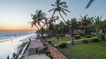 A beachfront property with a stone pathway leading to the beach, palm trees, and a small building with a tiled roof.
