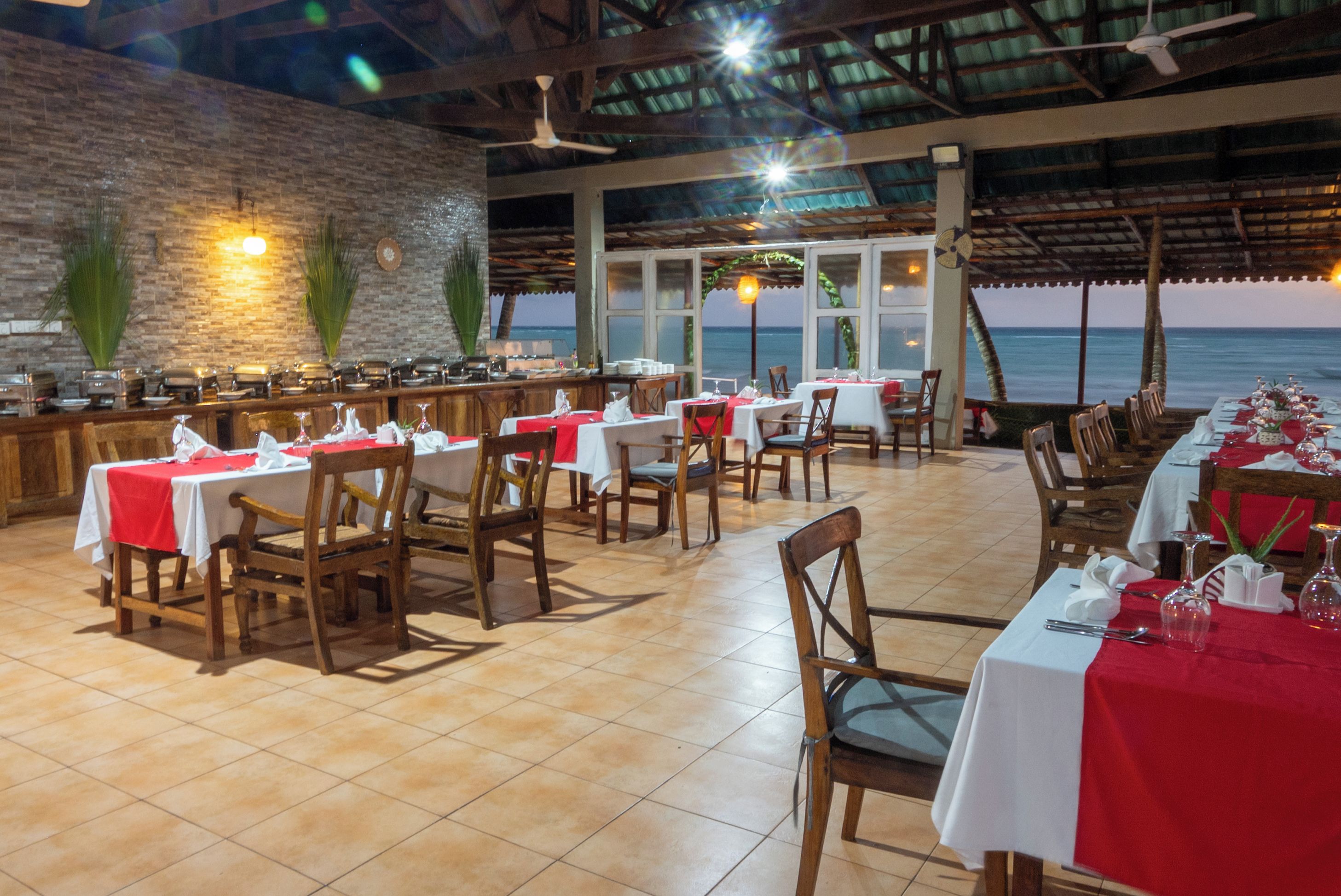 A restaurant with tables set for dining, a bar area, and a view of the ocean.
