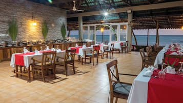 A restaurant with tables set for dining, a bar area, and a view of the ocean.