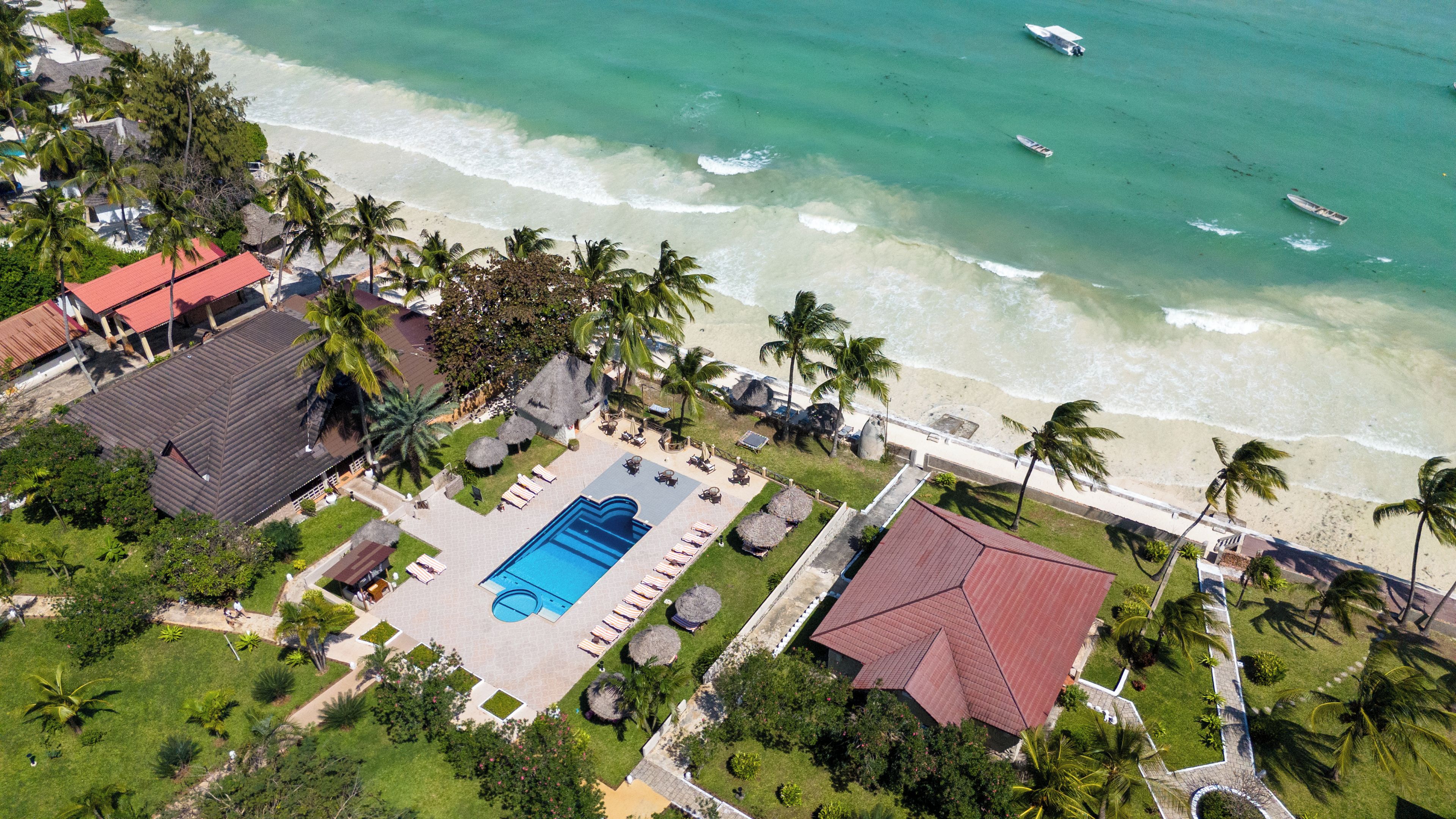 An aerial view of a resort with a swimming pool, beach access, and palm trees.