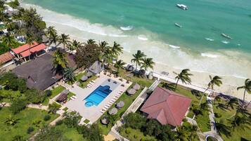 An aerial view of a resort with a swimming pool, beach access, and palm trees.