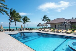 A swimming pool with lounge chairs and umbrellas, palm trees, and a view of the ocean. - Mandarin Resort Zanzibar (Kizimkazi)