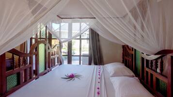 A bedroom with a canopy bed, wooden headboard, and a view of the outdoors.