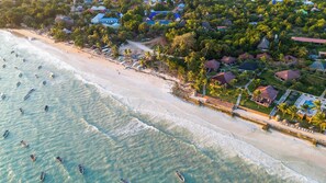An aerial view of a beach with boats, a sandy shore, and buildings with red roofs. - Mandarin Resort Zanzibar (Kizimkazi)