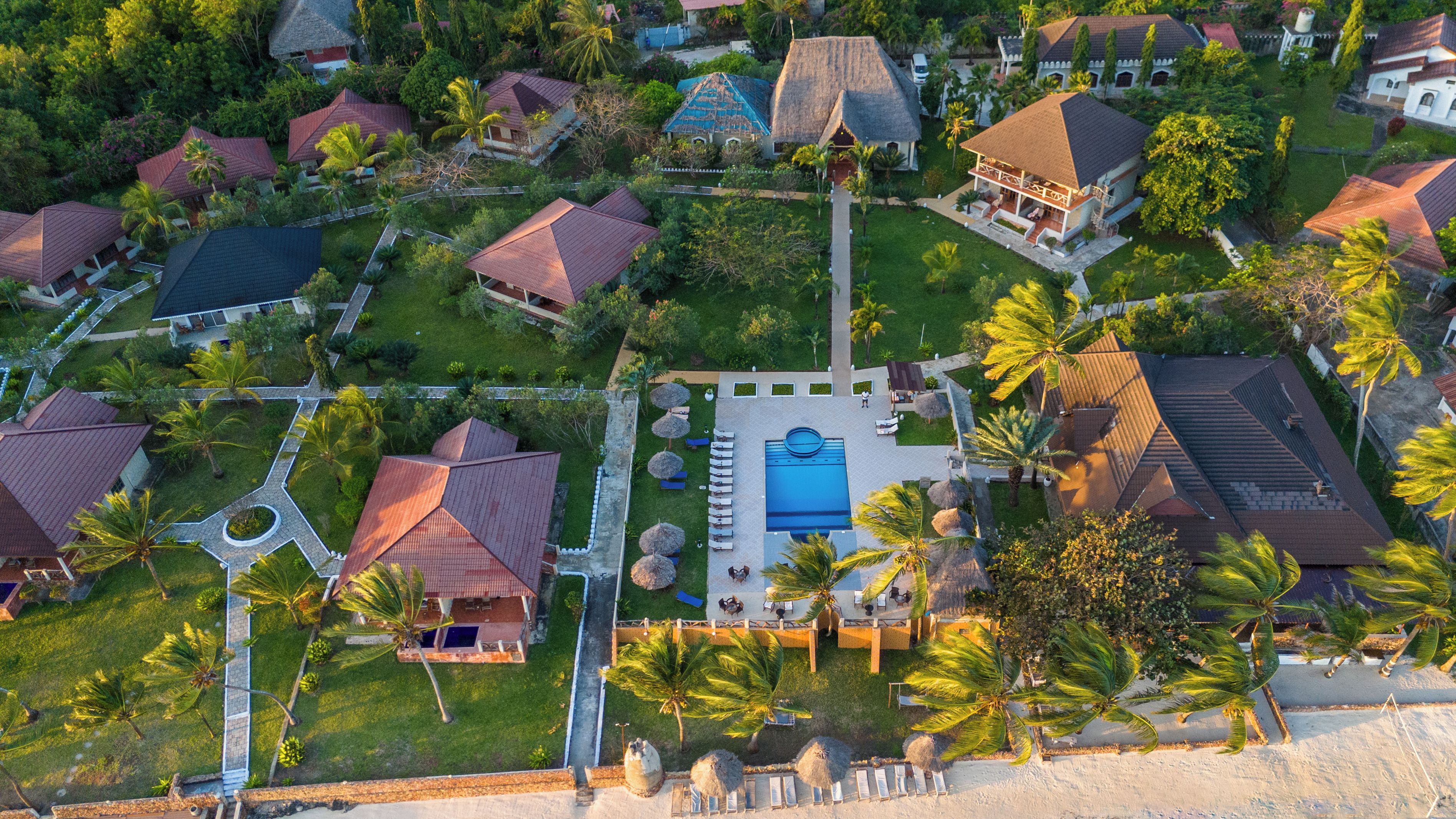 Vista aerea di un resort con diversi edifici, una zona piscina centrale e palme circostanti.
