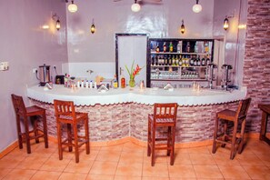A bar area with a curved counter, wooden chairs, and a shelf with bottles. - Mandarin Resort Zanzibar (Kizimkazi)