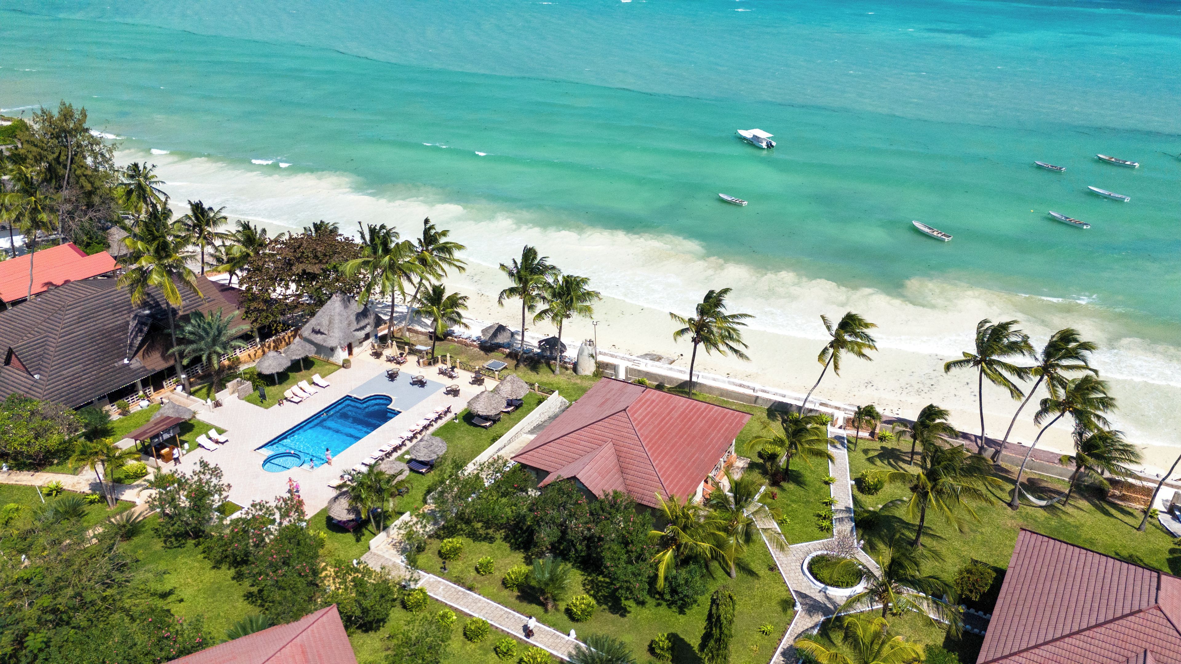 An aerial view of a resort with a swimming pool, beach, and palm trees.