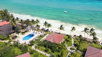 An aerial view of a resort with a swimming pool, beach, and palm trees.