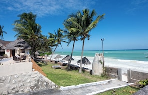A beachfront property with a patio area, palm trees, and a view of the ocean. - Mandarin Resort Zanzibar (Kizimkazi)