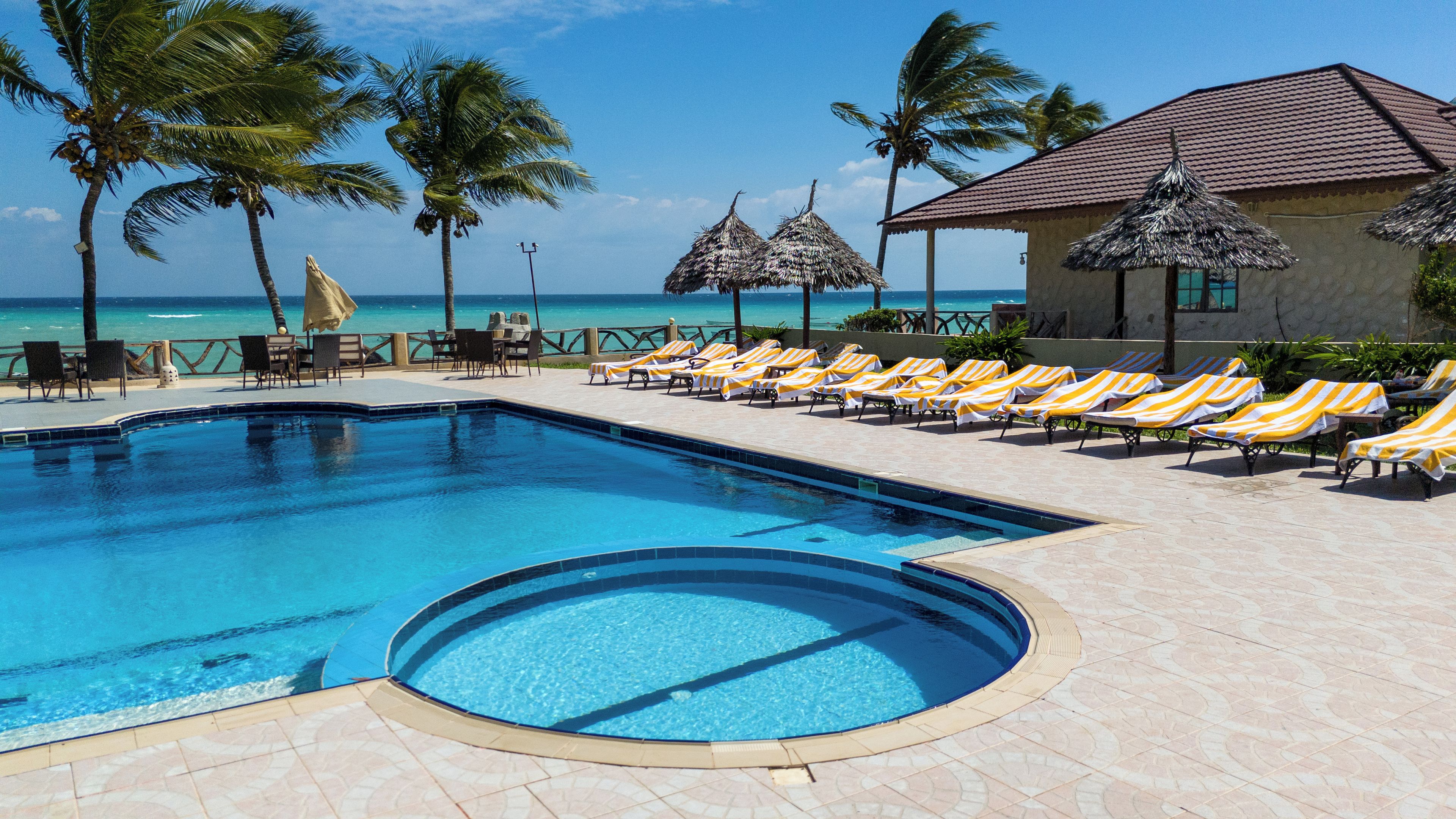 A pool with lounge chairs and palm trees, overlooking the ocean.