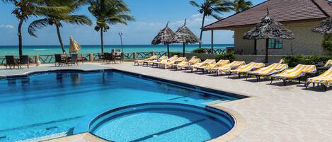 A pool with lounge chairs and palm trees, overlooking the ocean.