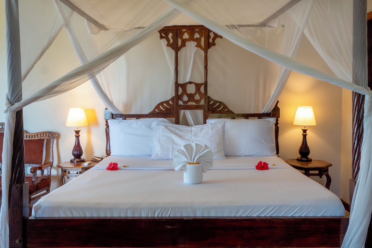 A large bed with a canopy, two bedside lamps, and a wooden headboard.