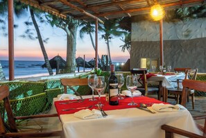 Tavola imbandita per la cena con vista sull'oceano e palme al tramonto.