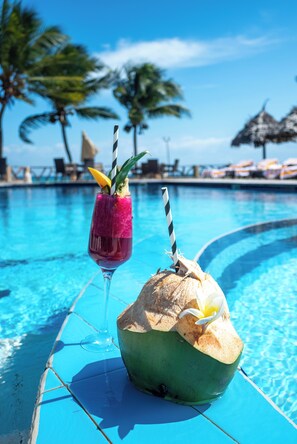 Un cadre agréable au bord de la piscine, avec un verre à la main et une noix de coco munie d’une paille.