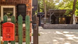 Un bâtiment en briques avec une boîte aux lettres, une clôture en bois et un espace extérieur aménagé avec des sièges.