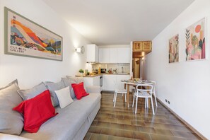 A compact living space with a kitchenette, a dining area, and a sofa with red pillows. - Appartamento Rio Secco with Balcony + Ski Storage, Claviere, Italy (Claviere)