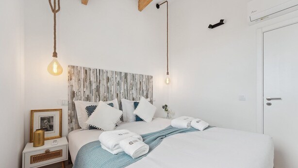 Une chambre à coucher bien rangée, avec un lit, des tables de chevet et un climatiseur fixé au mur.